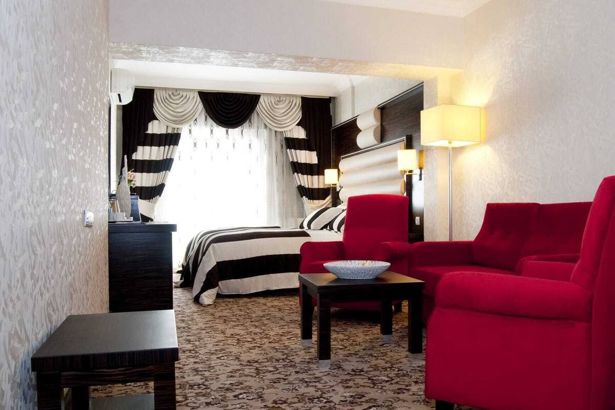 A hotel room with a bed, a red armchair, a small table, and a lamp.