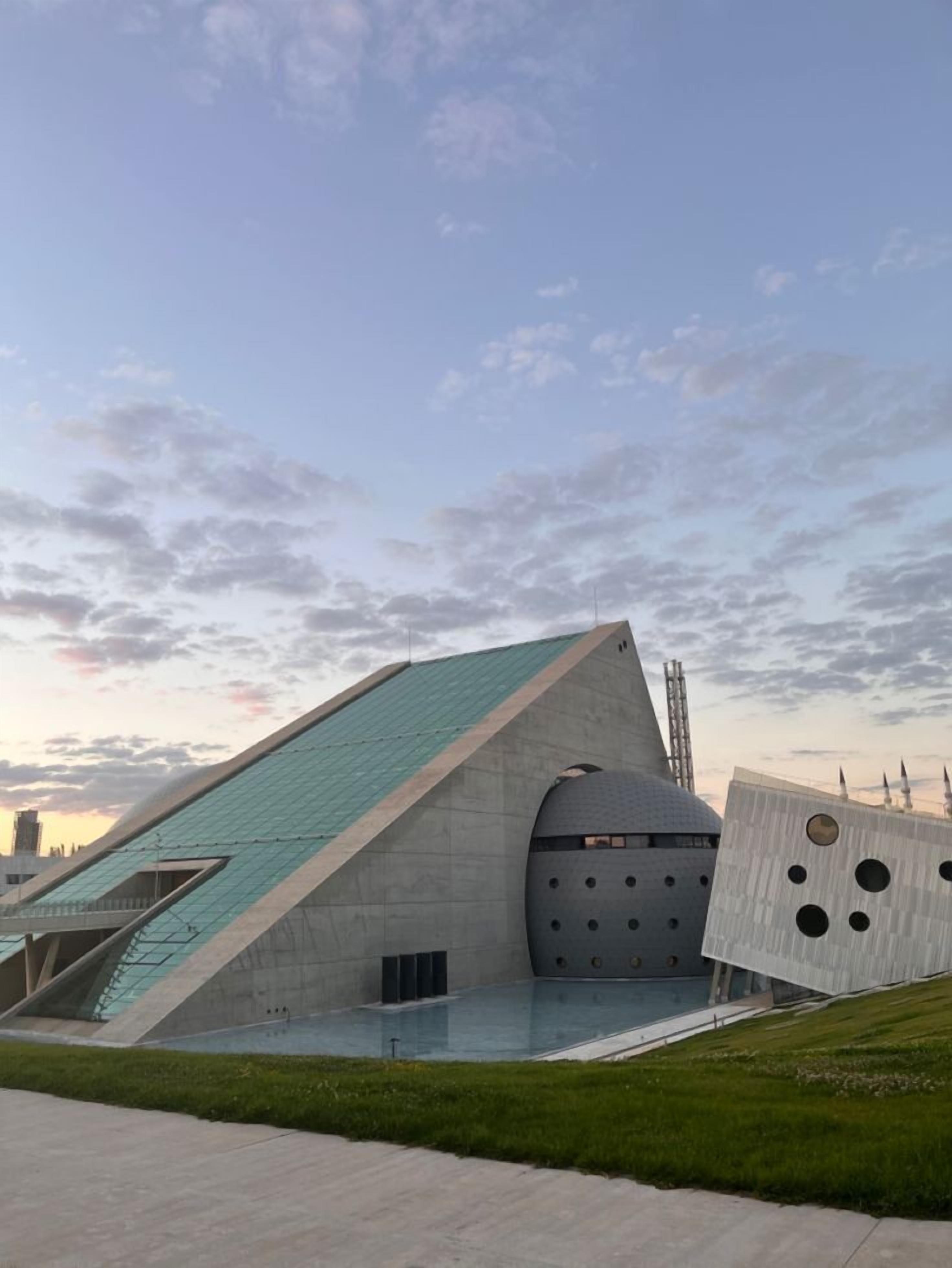 A modern building with a unique angular design, featuring a large glass facade and a green roof.