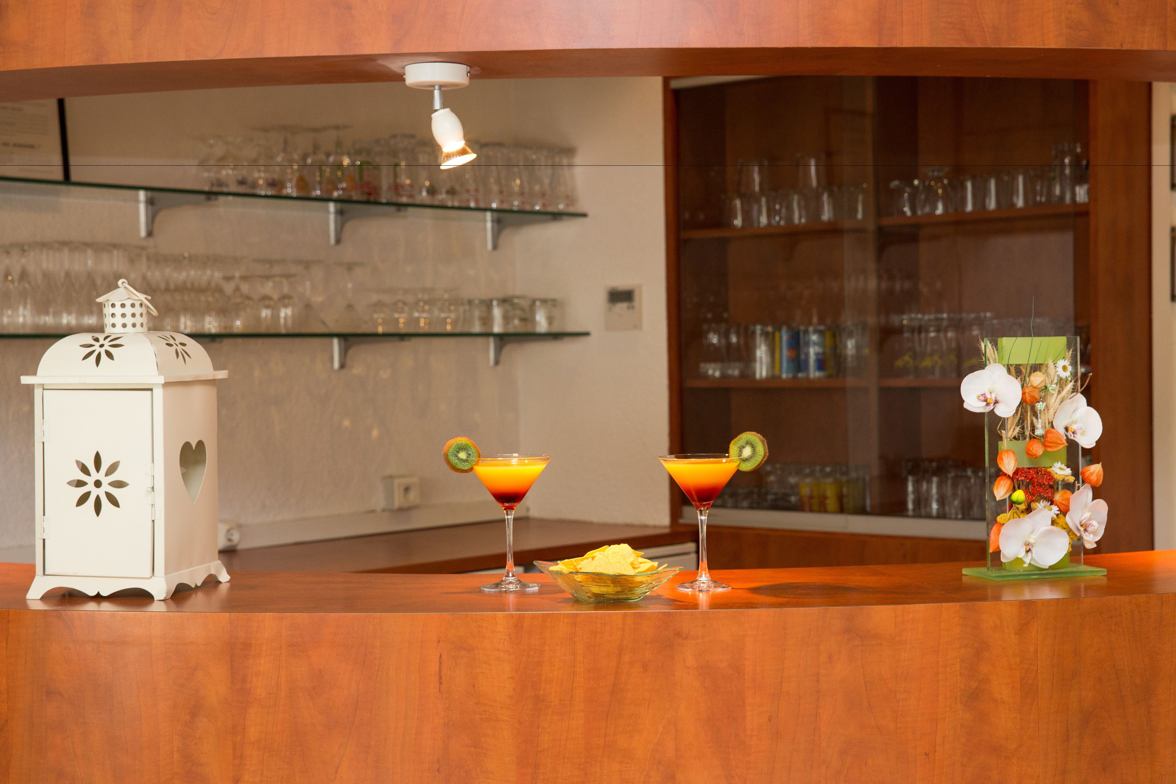 Una zona de bar con dos cócteles adornados con kiwi, un farol decorativo y un arreglo floral.