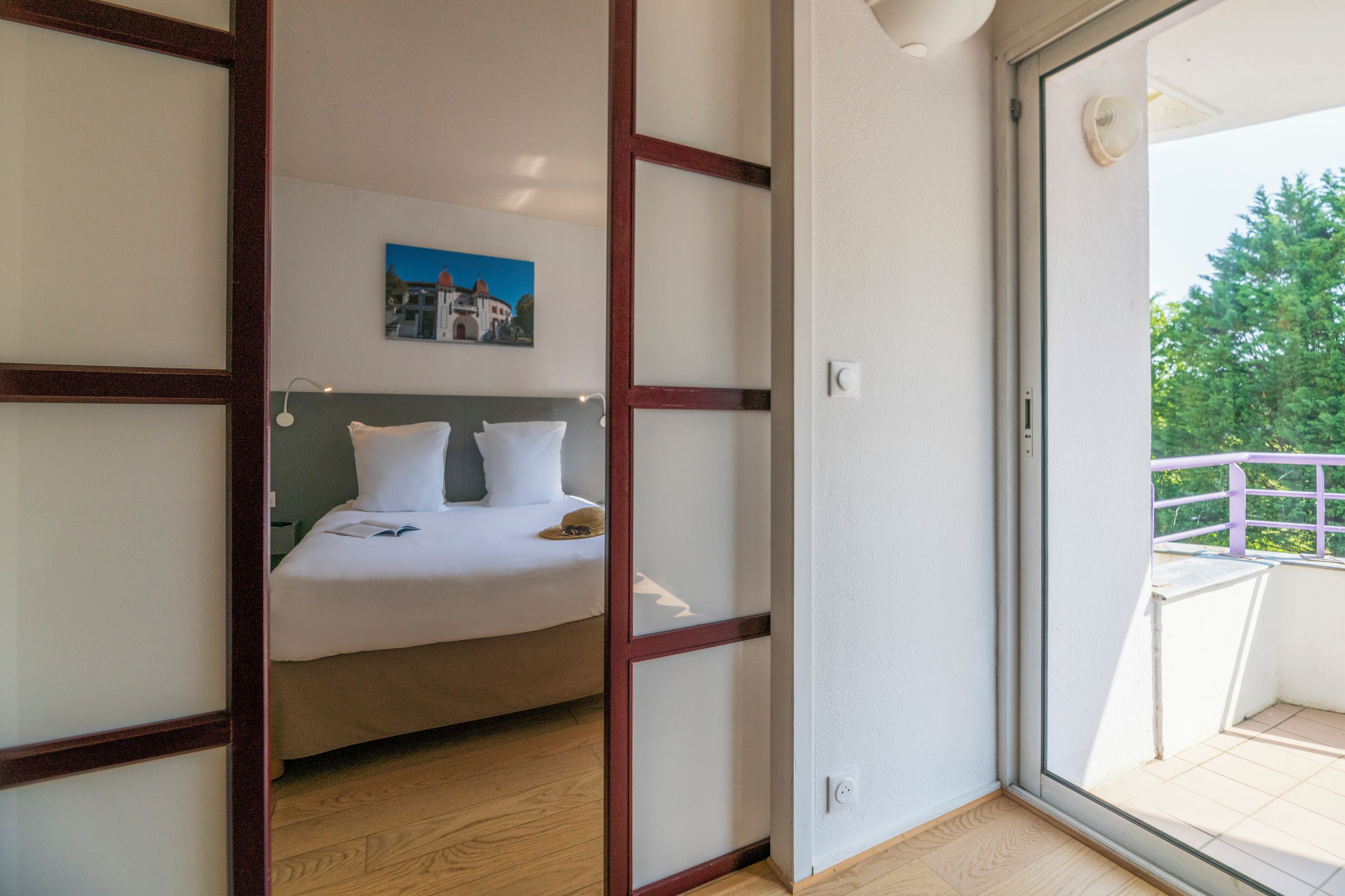 A bedroom with a bed, a painting on the wall, and a balcony with a railing.
