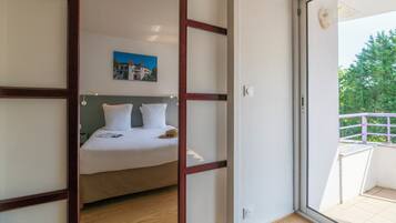 A bedroom with a bed, a painting on the wall, and a balcony with a railing.