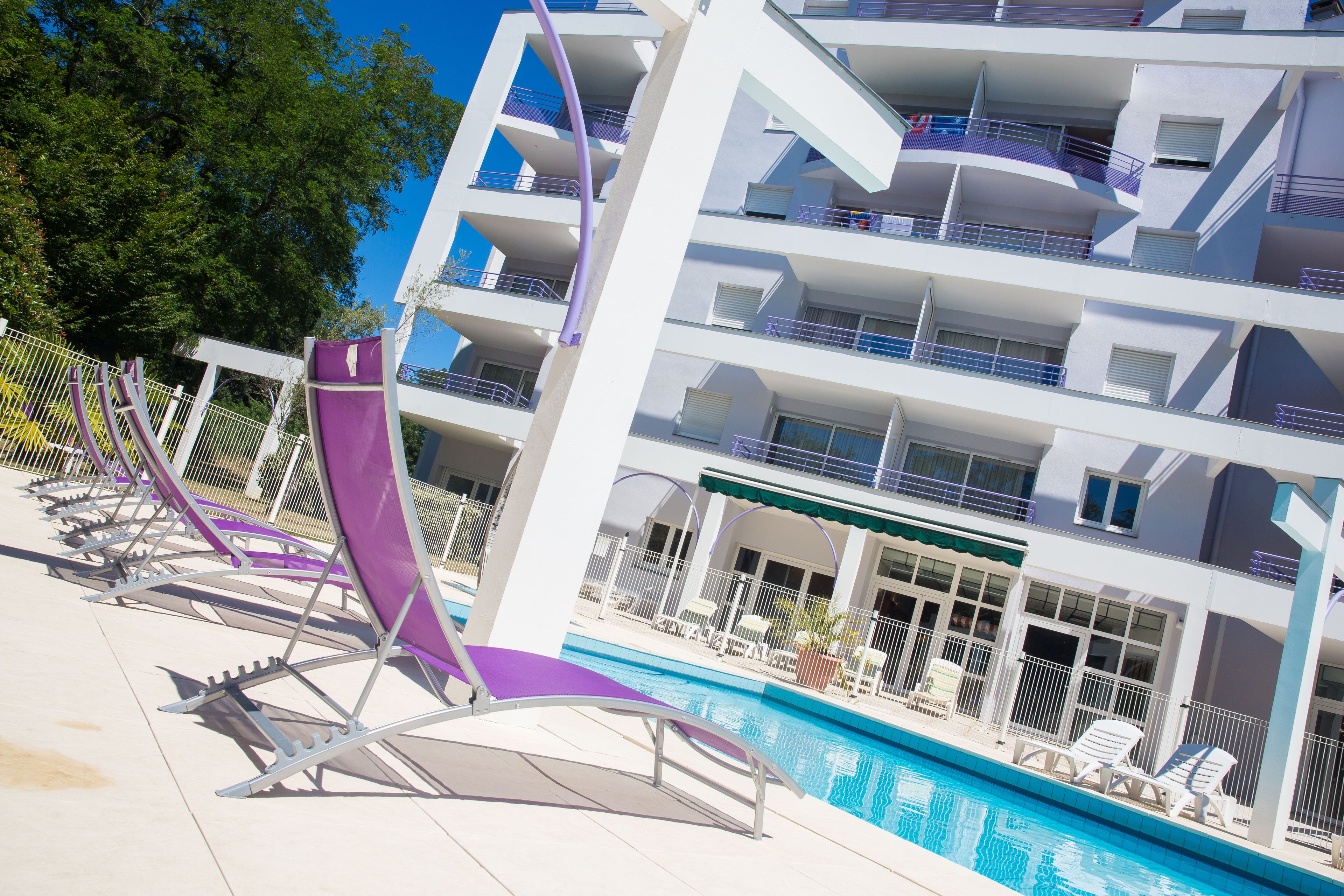 A modern hotel with a pool area, multiple balconies, and outdoor seating.