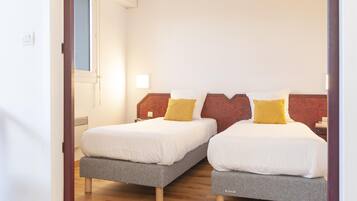 A room with two beds, each with a grey base and white bedding, and a wooden floor.