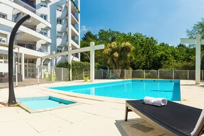 Una piscina con una silla de descanso y una toalla, rodeada por una valla y follaje.
