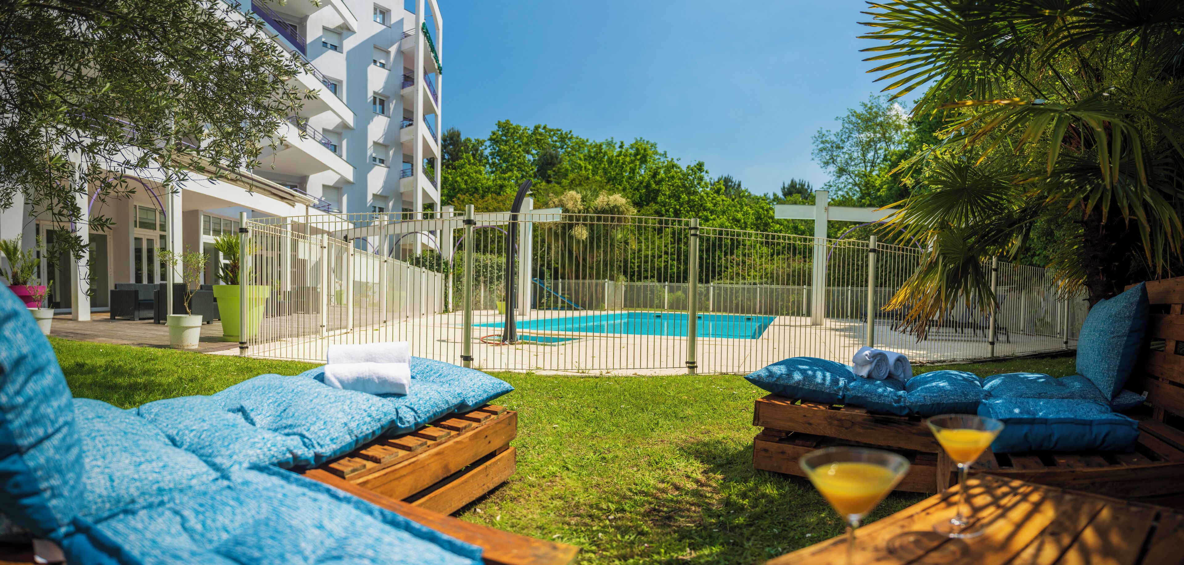 A pool area with lounge chairs and a wooden table with a drink.