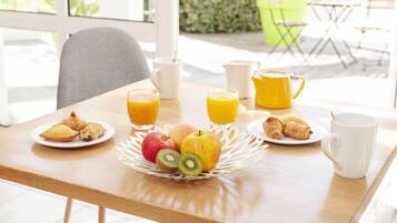 A breakfast table with croissants, apples, kiwi, and orange juice.