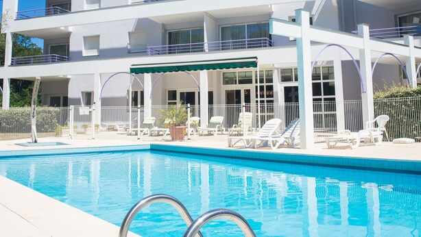 A multi-story hotel with a swimming pool, balconies, and outdoor seating. - CERISE Dax - Les Jardins du Lac (Saint-Paul-les-Dax)