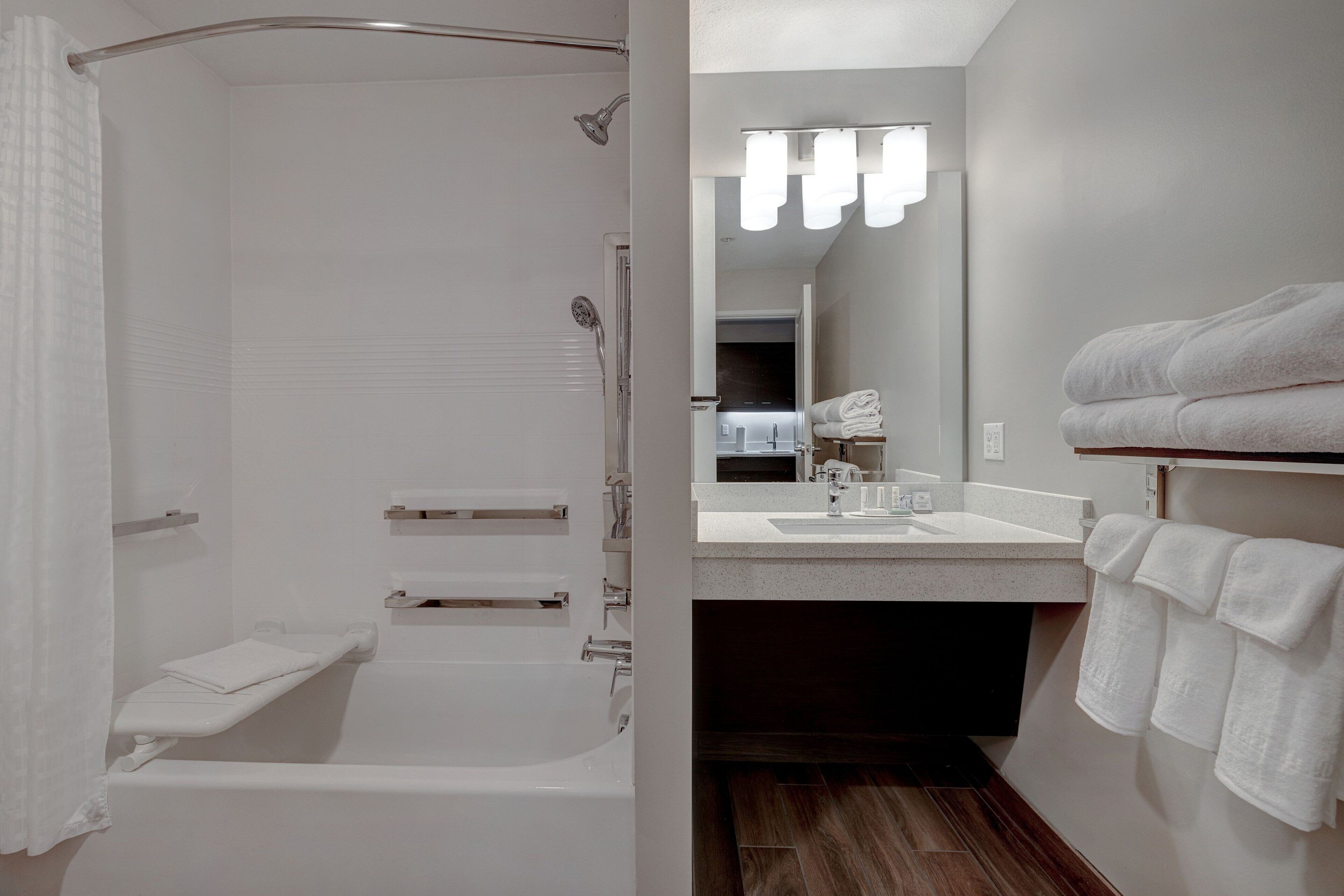 Un bagno moderno con doccia, lavandino e specchio. Asciugamani a parete e pensile con articoli da toilette.