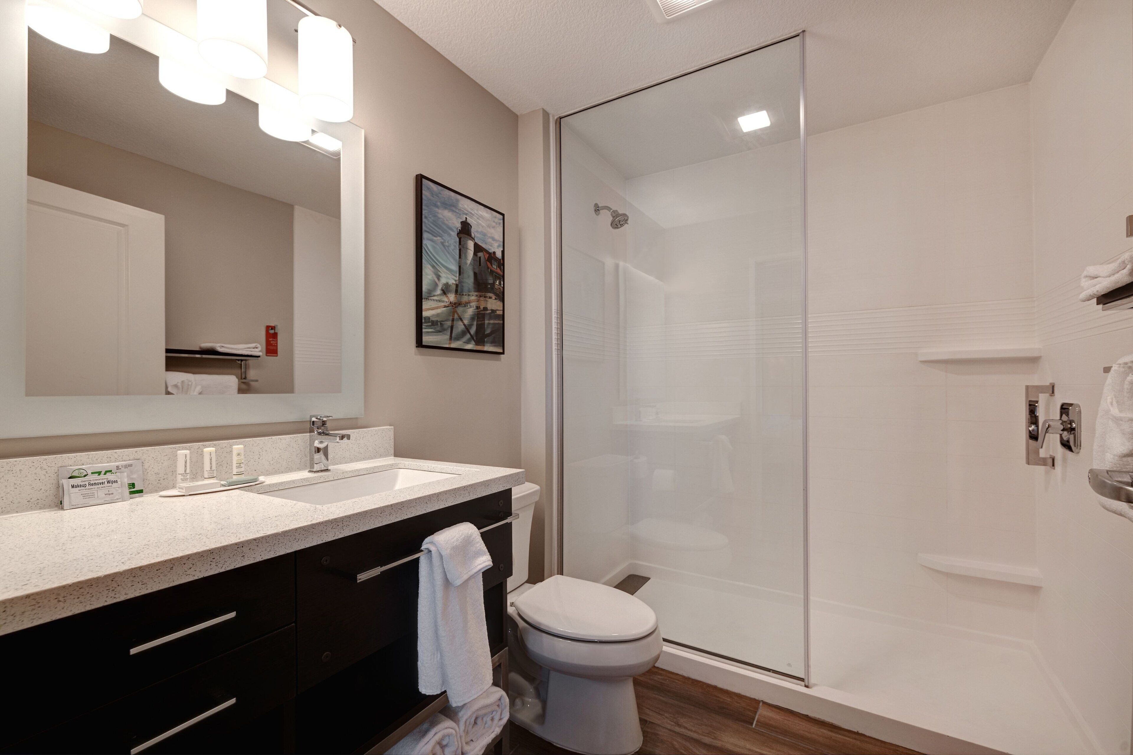 Une salle de bain moderne avec une douche à parois de verre, des toilettes blanches et un meuble-lavabo doté d’un miroir et d’un plan de travail.