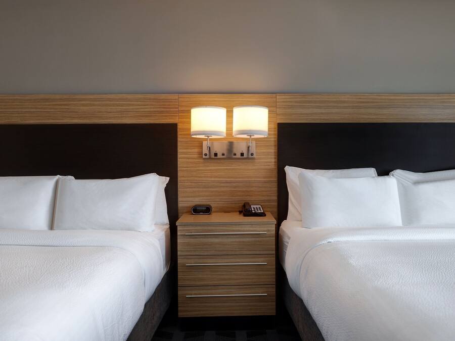 A hotel room with two beds, a wooden headboard, a nightstand with a lamp, and a phone.