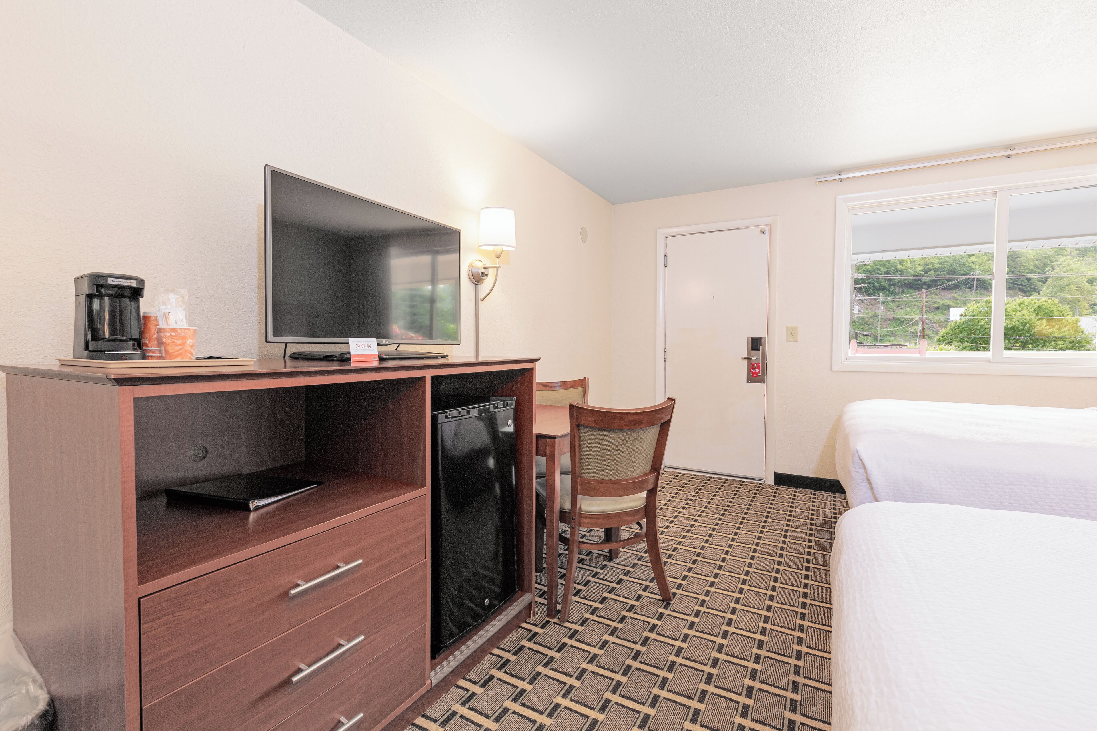 A hotel room with a bed, a desk with a television, a coffee maker, and a chair.