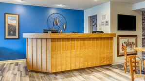 A reception area with a wooden counter, blue walls, a mounted TV, and a dining area with wooden chairs. -  Econo Lodge Cherokee Near Island Park (Cherokee)