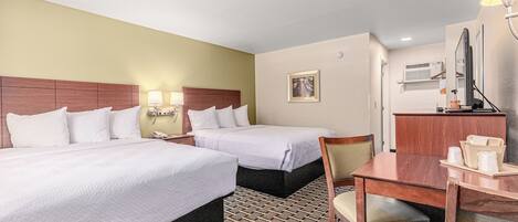 A hotel room with two beds, a desk, a chair, a lamp, a mirror, and a picture on the wall.