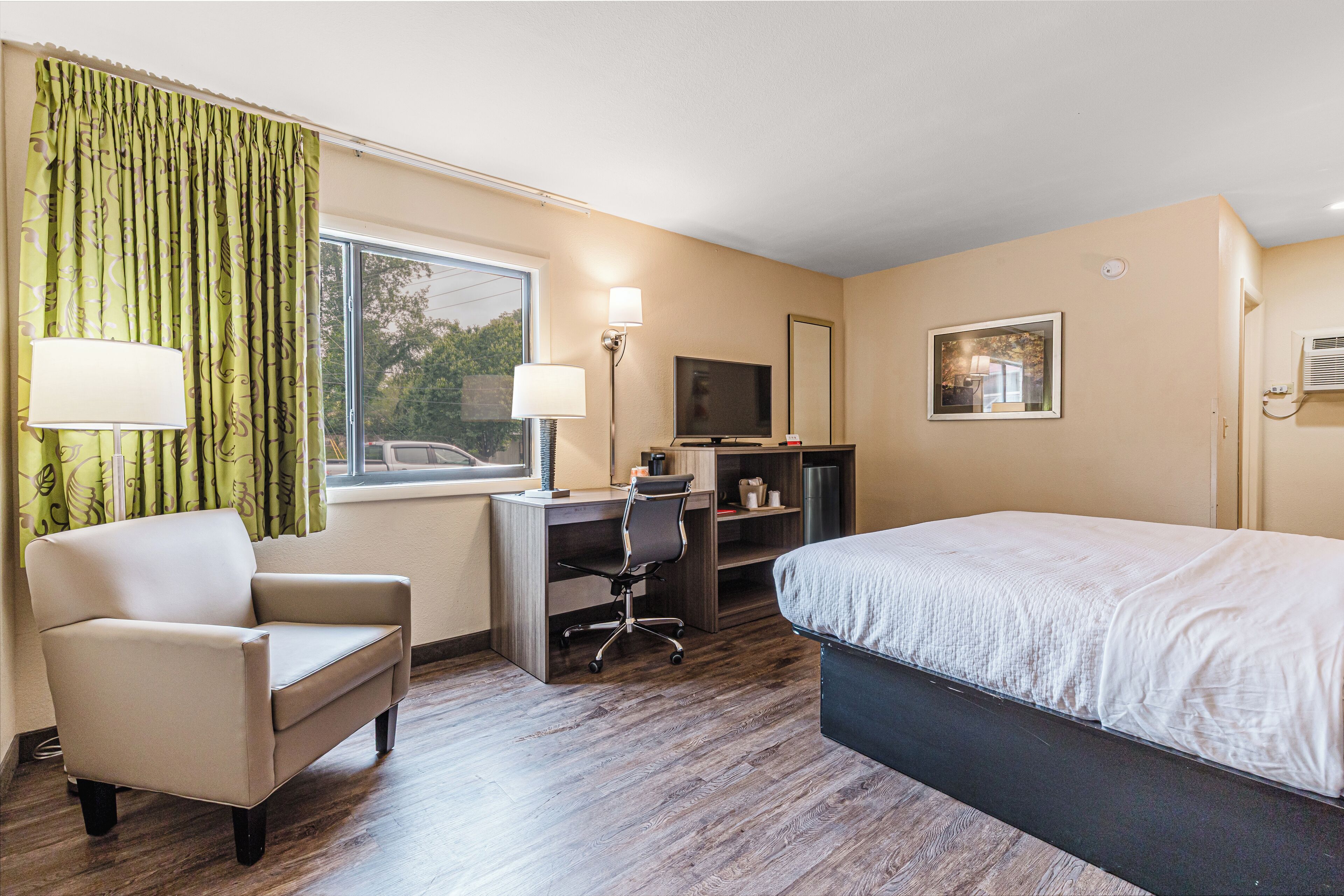 A hotel room with a bed, a desk with a chair, a television, and a window with curtains.