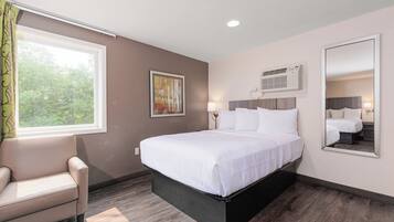 Ein Hotelzimmer mit einem großen Bett, einem Sessel, einem Fenster mit Vorhängen, einem Gemälde und einer Klimaanlage.