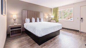 A hotel room with a large bed, bedside lamps, a nightstand, and a window with a view of a staircase. -  Econo Lodge Cherokee Near Island Park (Cherokee)