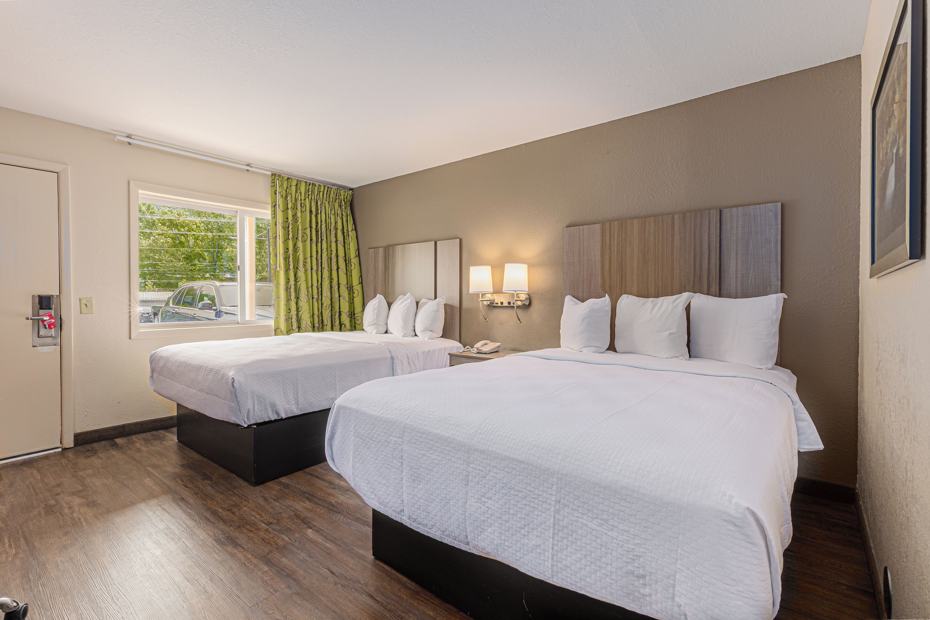 Habitación de hotel con dos camas, una ventana con cortinas, un teléfono sujeto a la pared y una mesita de noche con lámpara.
