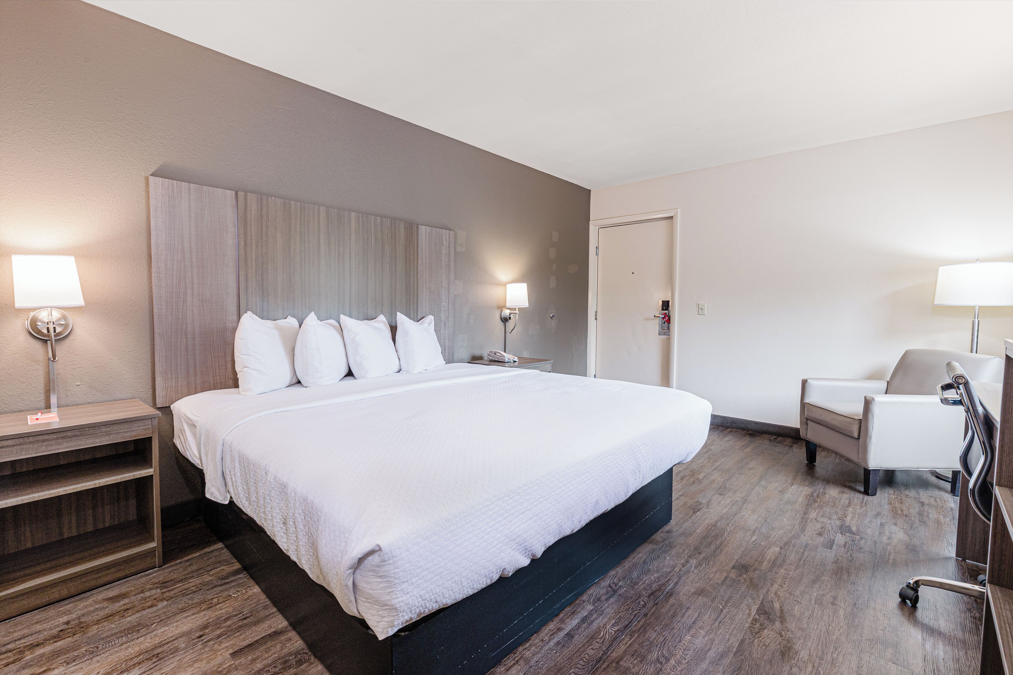 A hotel room with a large bed, two bedside tables with lamps, a chair, and a desk with a chair.
