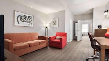 A modern hotel room with a sofa, armchair, and a desk with a chair.
