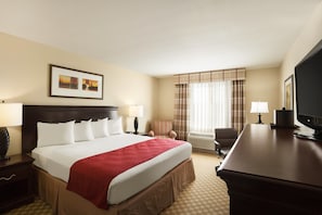 A hotel room with a large bed, a desk, a chair, a television, and a window with curtains.