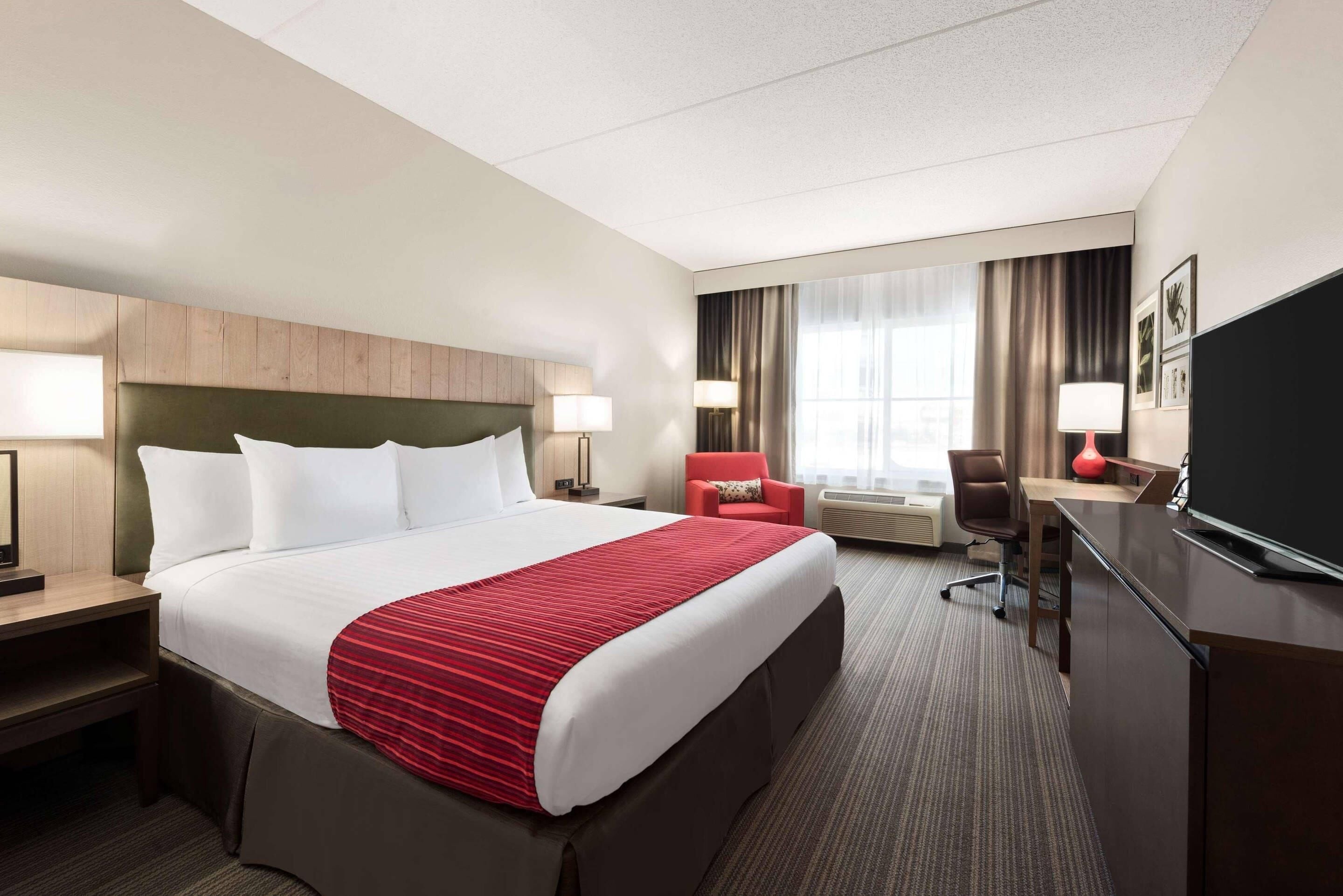 A hotel room with a large bed, a desk, a chair, a TV, and a window with curtains.