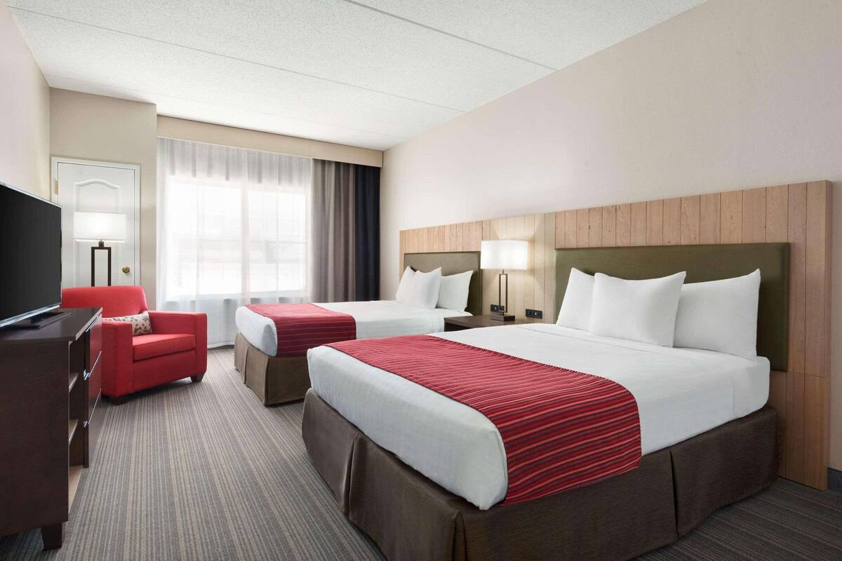 A hotel room with two beds, a desk, a TV, and a red armchair.