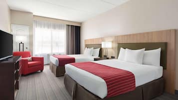 Een hotelkamer met twee bedden, een bureau, een televisie en een rode stoel.