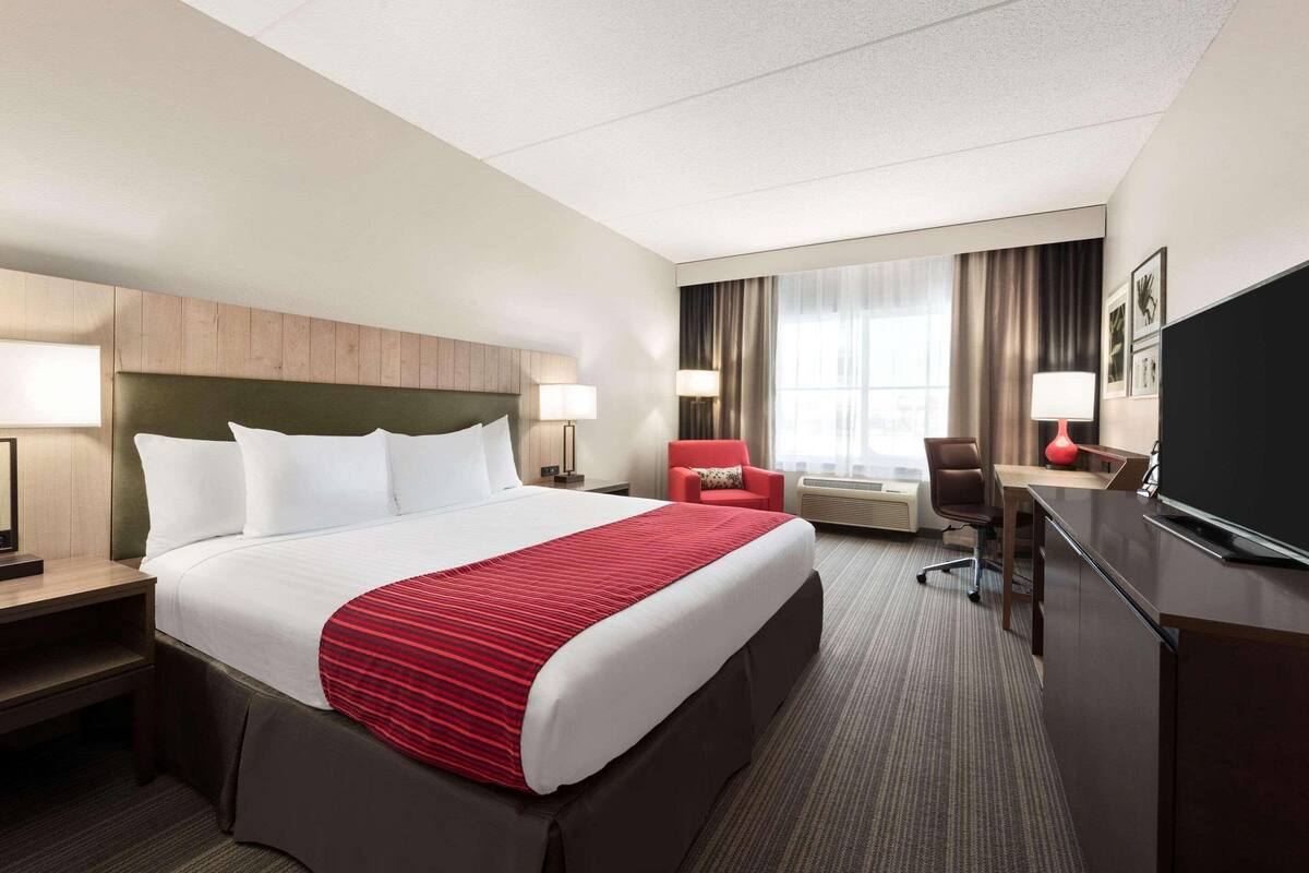 A hotel room with a large bed, a desk, a television, and a chair.
