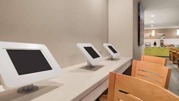 A counter with three digital kiosks, a wooden chair, and a glimpse of a kitchen area in the background.