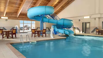 An indoor swimming pool with a blue water slide and a seating area with chairs and tables.