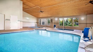 Una piscina interior con techo de madera, ventanas de vidrio transparente y suelo de baldosas.