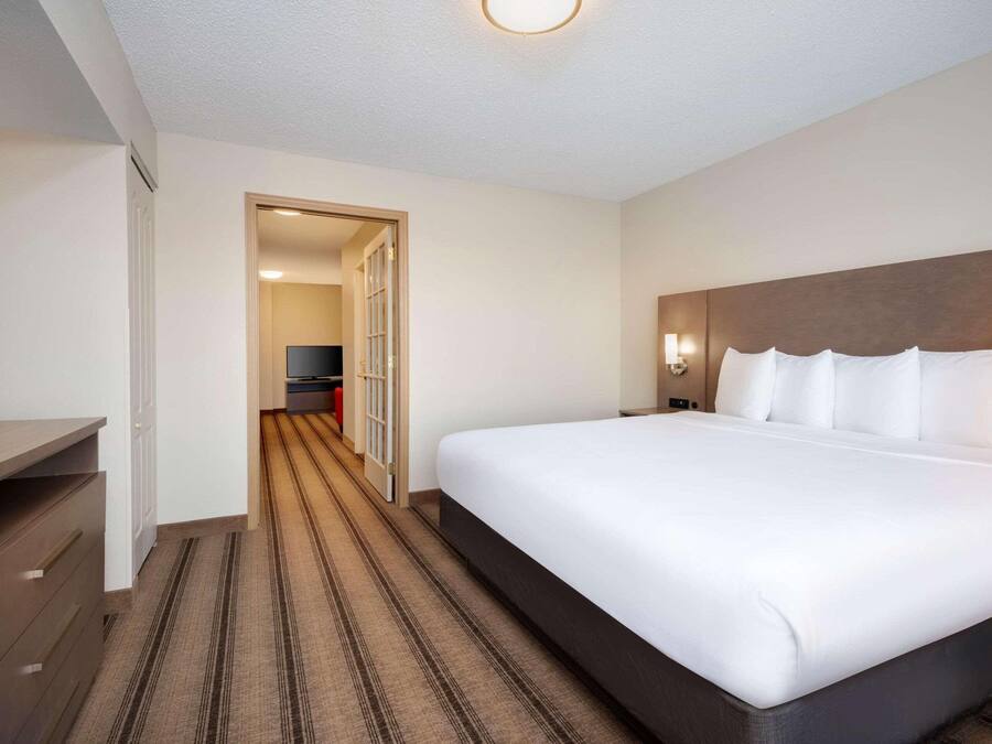 A hotel room with a large bed, a TV on a desk, and a door leading to a hallway.