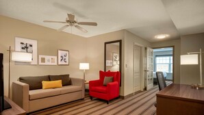 Una habitación de hotel con un sofá, un sillón rojo, un escritorio y un ventilador de techo.