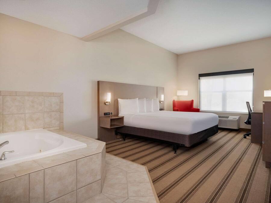A hotel room with a large bed, a separate bathroom with a bathtub, a flat-screen TV, and a large window.