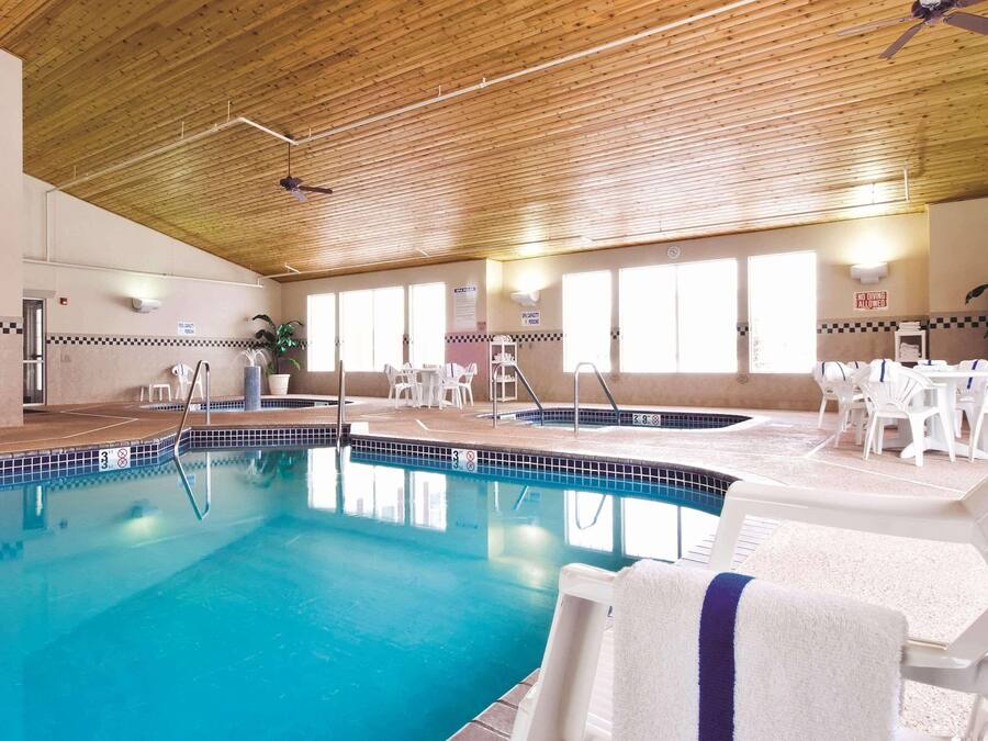 An indoor swimming pool with a wooden ceiling, multiple windows, and white lounge chairs with towels.