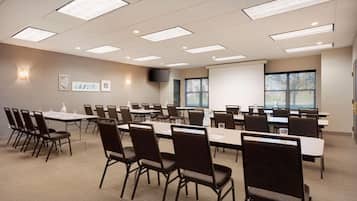 A conference room with multiple tables and chairs, a projector screen, and a television on the wall.