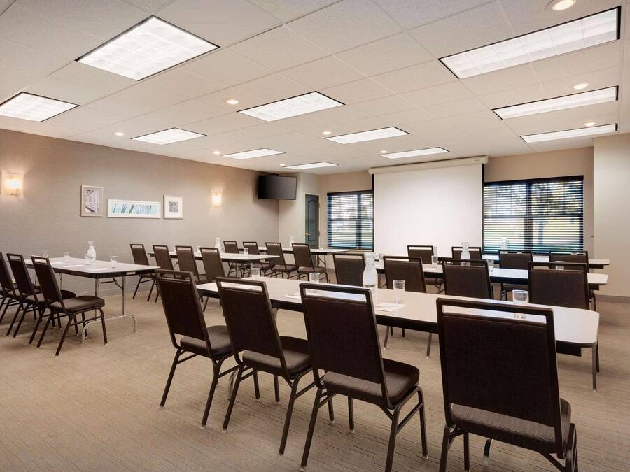 A conference room with multiple tables and chairs, a projector screen, and a television on the wall.