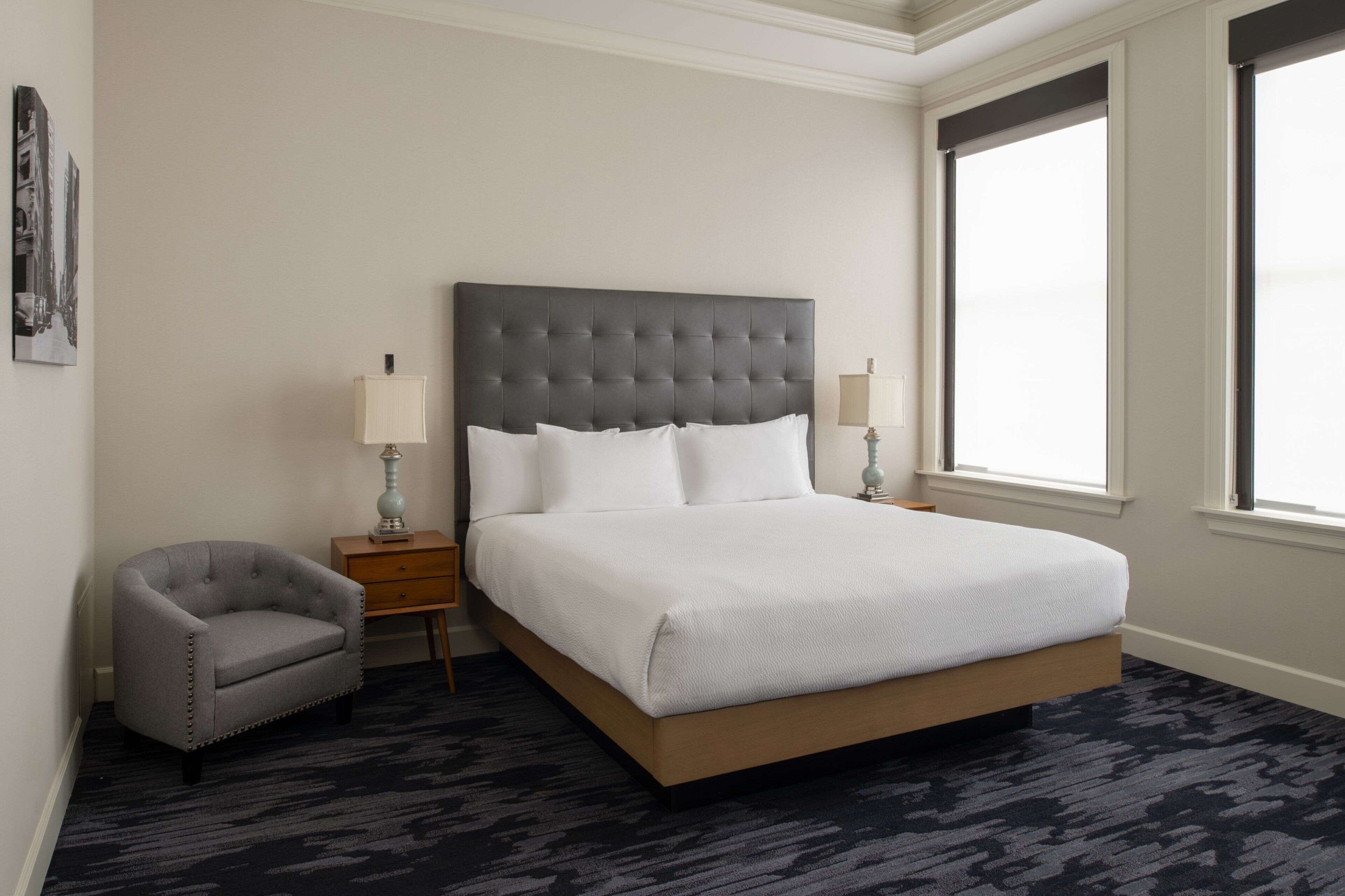 A neatly arranged hotel room with a large bed, two bedside tables, a chair, and a window.