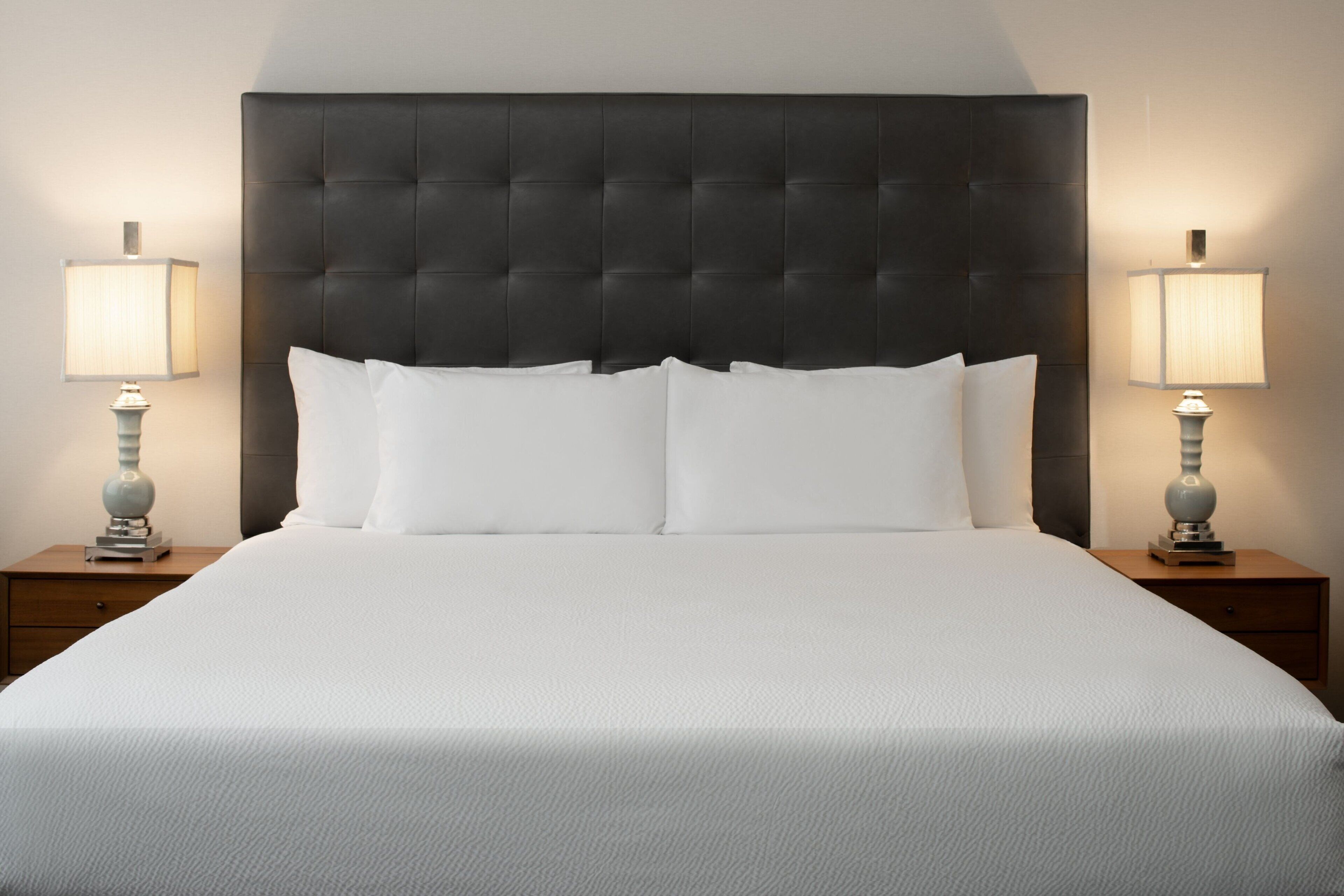 Una cama grande con cabecera capitonada, dos mesitas de noche con lámparas y una pared en tonos neutros.