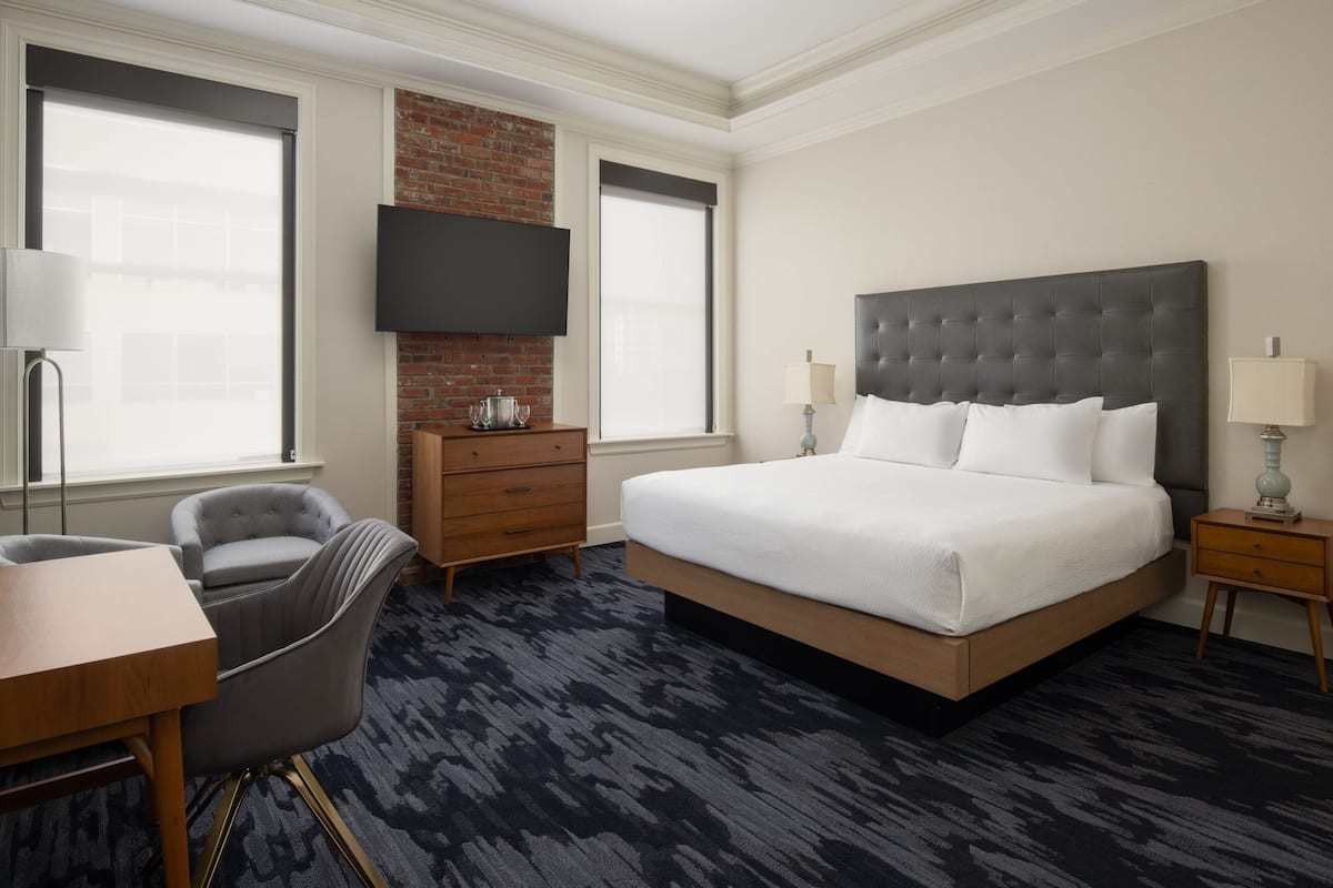 Een hotelkamer met een groot bed, een flatscreen televisie aan de muur, een bureau met stoel, en een raam met uitzicht op de stad.