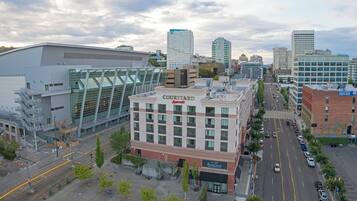 Un hotel Courtyard by Marriott con fachada de vidrio, situado en una ciudad con edificios altos y una calle concurrida.