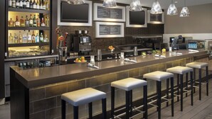 A modern bar area with a long counter, multiple stools, a selection of bottles, and a menu board. - Courtyard by Marriott Tacoma Downtown (Tacoma)