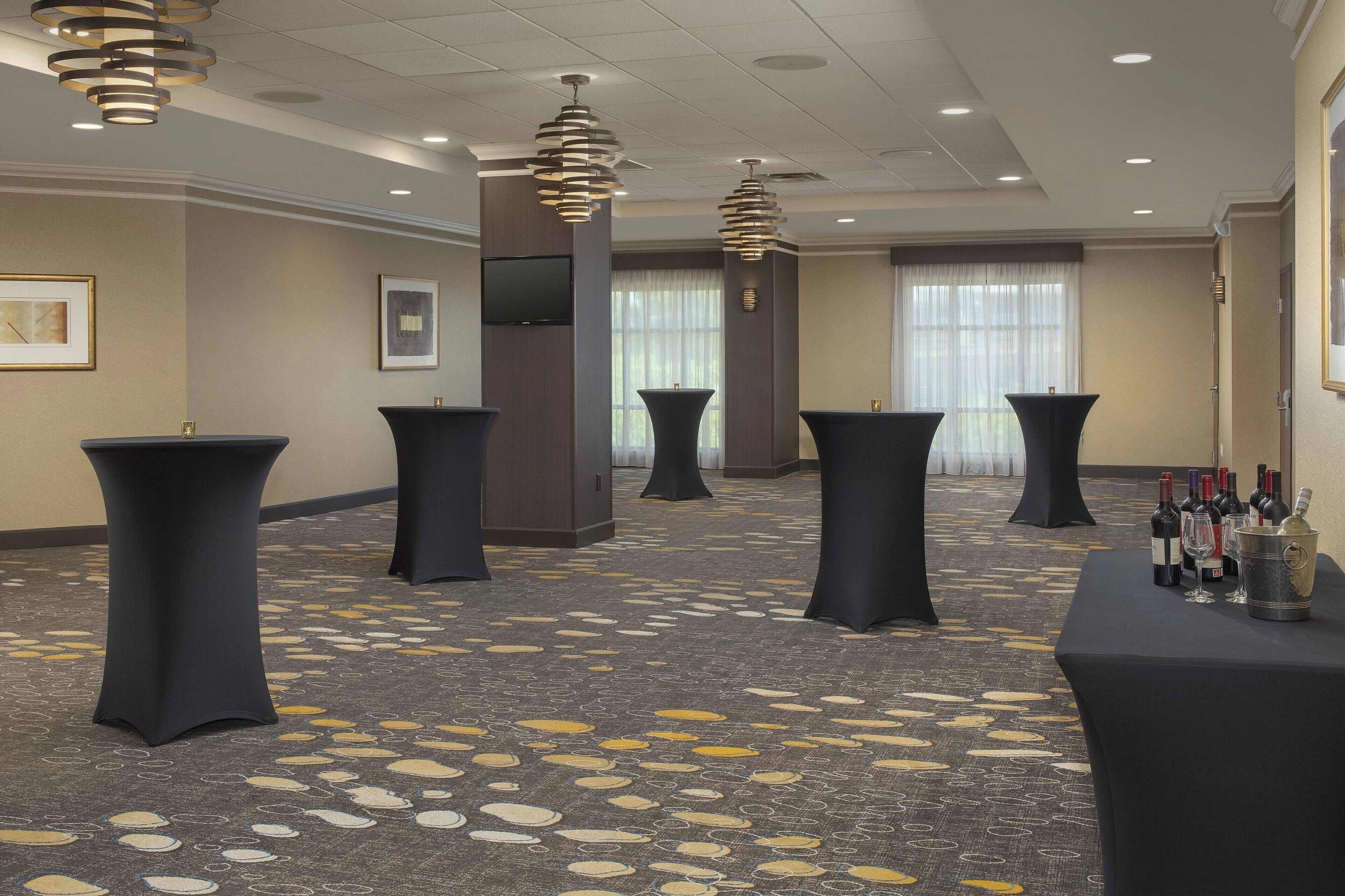 A hotel lobby with round tables, a flat-screen TV, and a carpet with a leaf pattern.