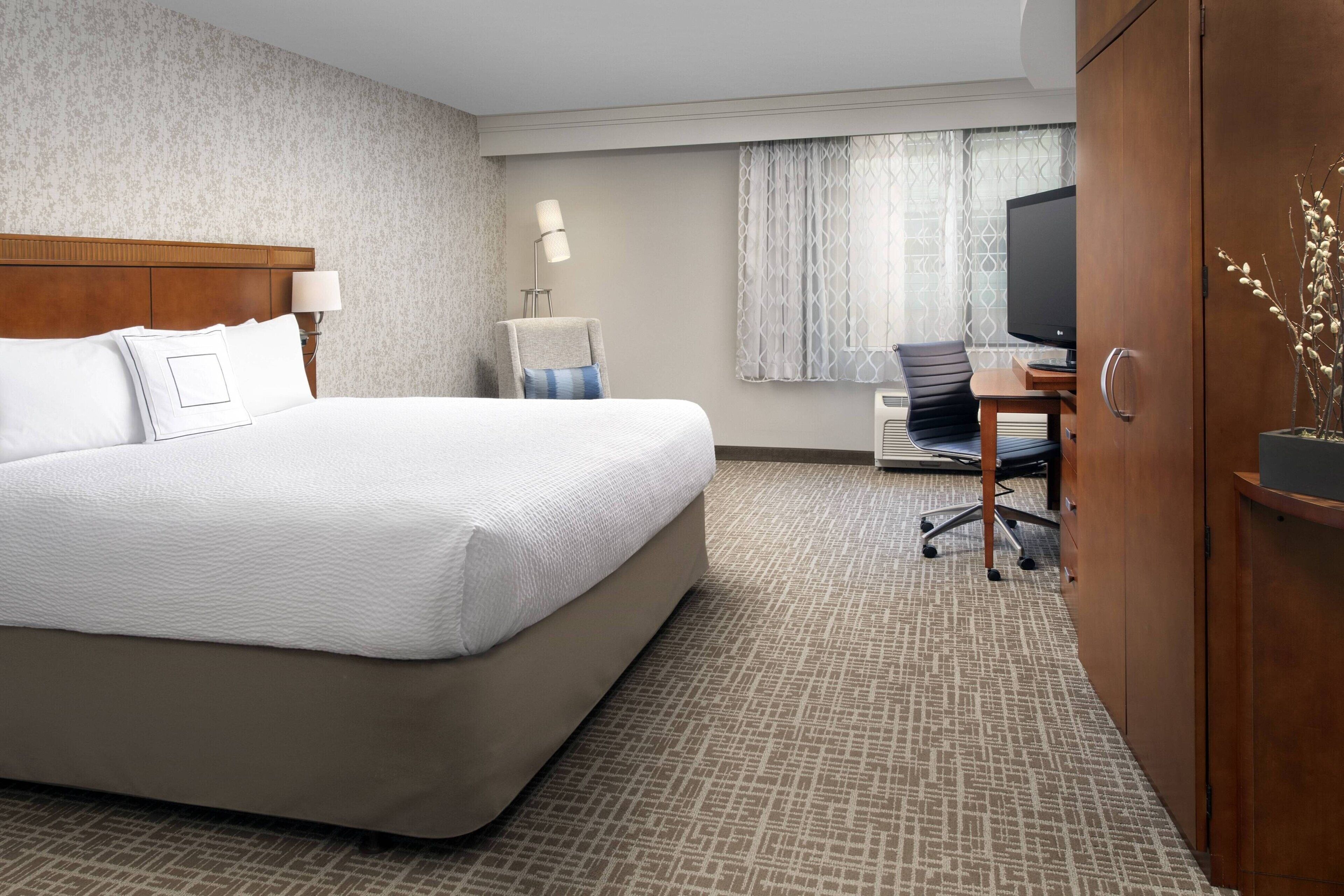 A hotel room with a large bed, a desk with a chair, a television, and a wardrobe.