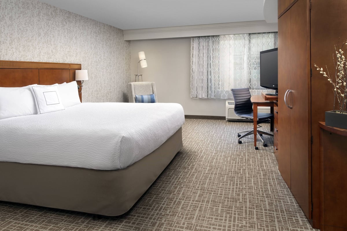 Een hotelkamer met een groot bed, een bureau met stoel, een televisie en een kledingkast.