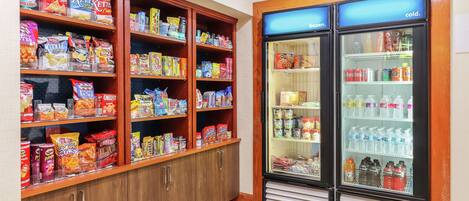 A snack and beverage section with shelves stocked with chips, snacks, and a refrigerator containing bottled water and soda.