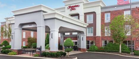 Un hôtel Hampton Inn avec une façade en briques, une entrée couverte et un drapeau américain.