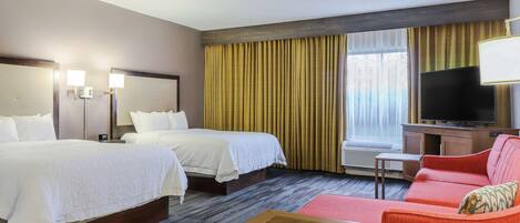 A hotel room with two beds, a TV, a sofa, and a small table.
