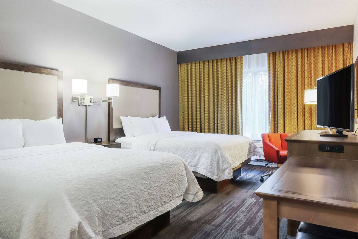 A hotel room with two beds, a desk, a chair, a TV, and curtains.