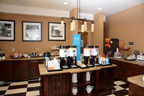A hotel kitchen with multiple coffee machines, a check-in counter, and framed pictures on the wall. - Hampton Inn Americus (Americus)